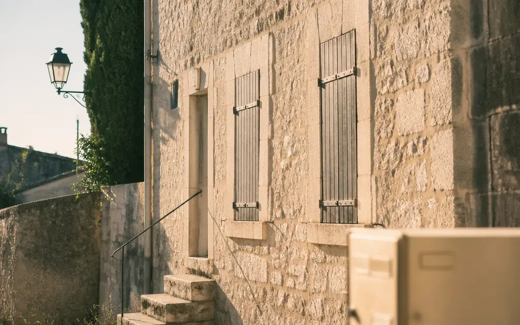 Maison de village en pierre à Roquefort-la-Bédoule, façade au soleil rasant, volets fermés, boîte aux lettres à deux…